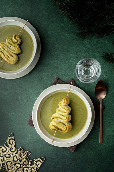 Weihnachtliche Draufsicht: Feldsalatsuppe mit Blätterteig-Tannenbaum auf Backdrop „Feldsalat" – dunkelgrüner Fotohintergrund mit Kupferlöffel und Tannenzweigen