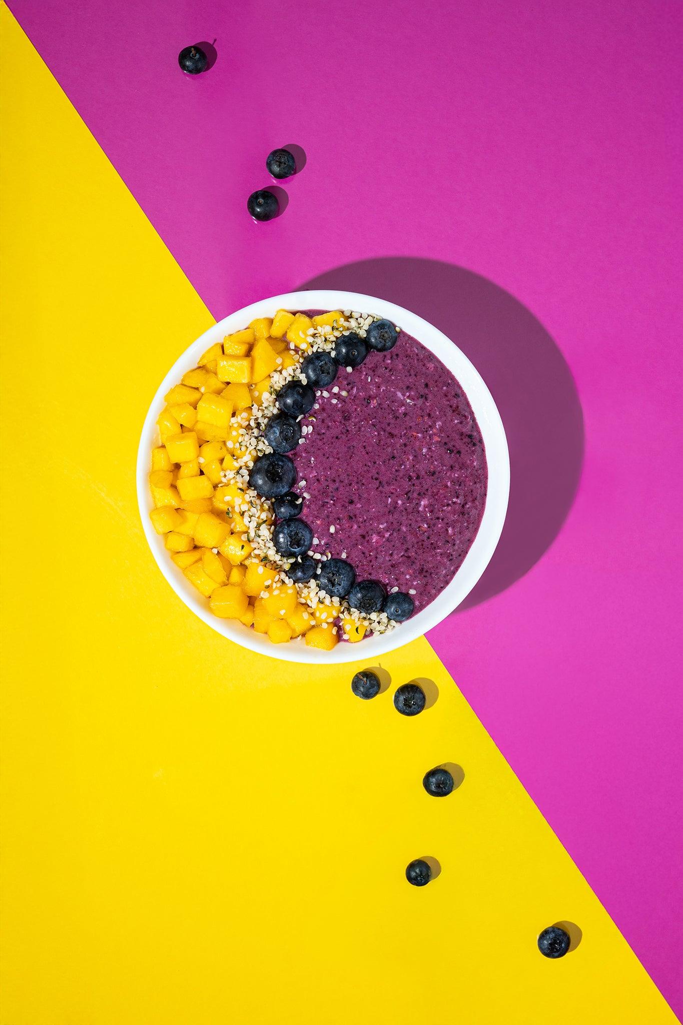 Foodfotografie Smoothie Bowl mit Blaubeeren und Mango auf Backdrop „Zitrone“ und „Granatapfel“ – gelber und pinker Fotohintergrund kombiniert